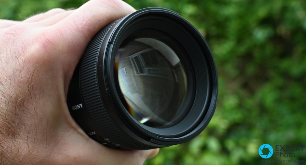 Lentille frontale Sony FE 85mm f/1.4 GM II vue de face, reflets arc-en-ciel, tenue en main, marquage SONY sur barillet.
