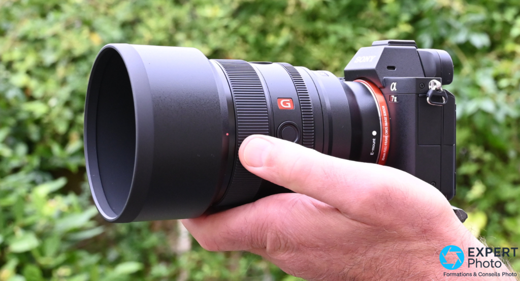 Sony FE 85mm f/1.4 GM II avec pare-soleil sur boîtier Sony Alpha 7 II, logo G rouge et E-mount visibles, tenu en main.