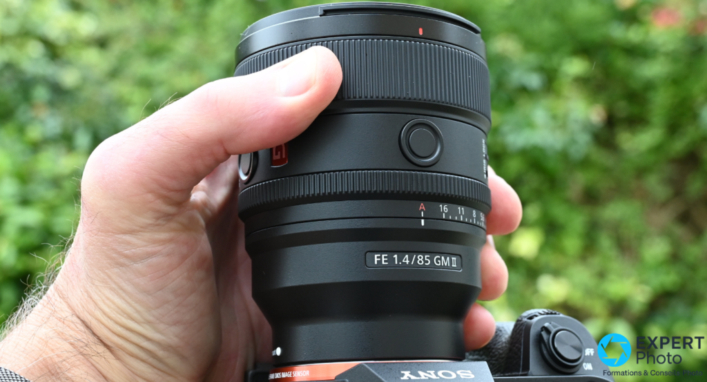 Sony FE 85mm f/1.4 GM II profil latéral tenu en main, bague de mise au point et graduation diaphragme, boîtier Sony visible.