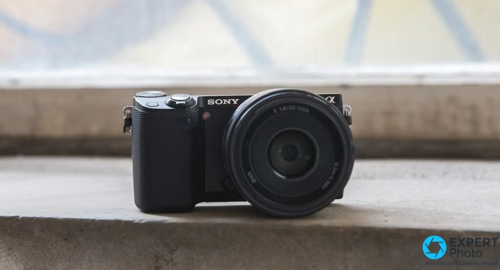 Sony NEX-5R noir de face avec objectif Sony E 35mm f/1.8 OSS monté, posé sur un rebord béton, fond flou 