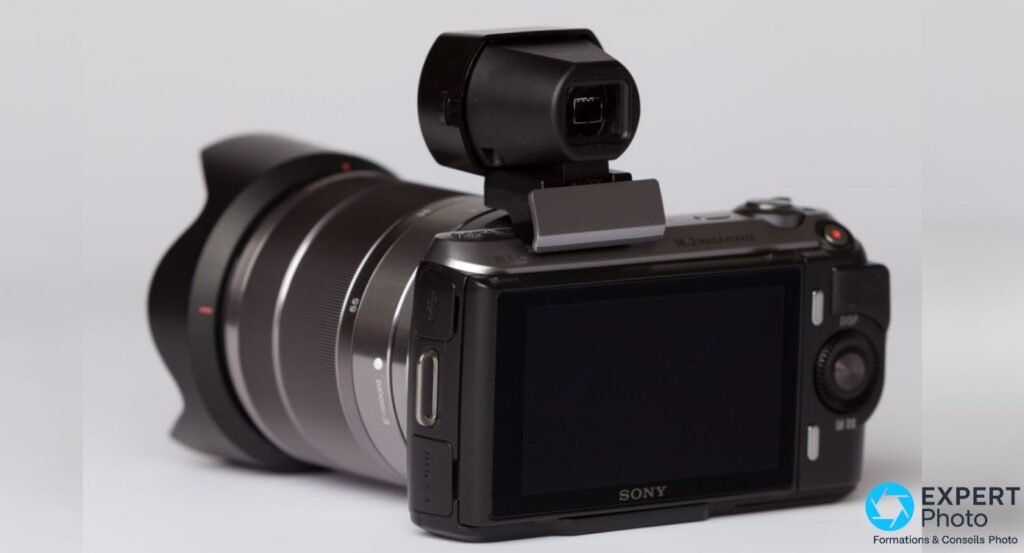 Sony NEX-C3 vue arrière 3/4, zoom Sony 18-55 mm monté avec pare-soleil, viseur externe noir sur griffe, écran 3" éteint.