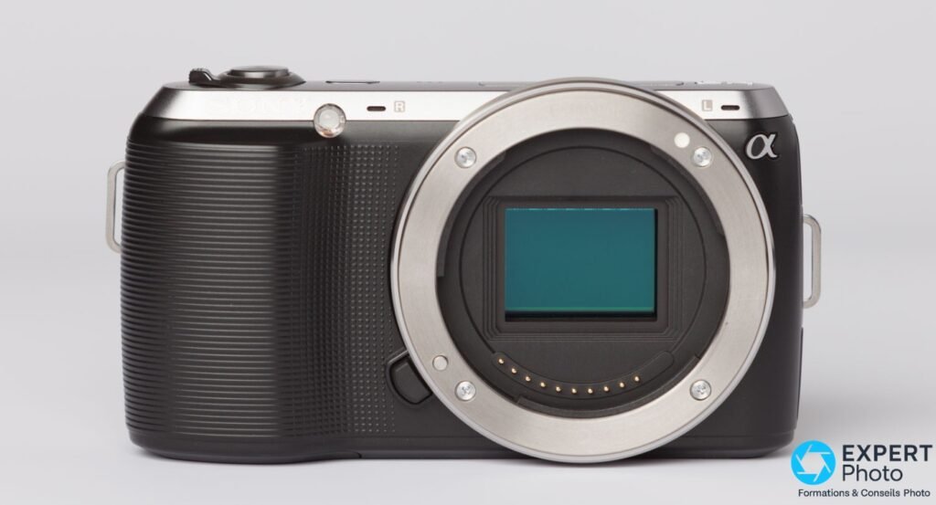 Sony NEX-C3 nu face avant, monture Sony E ouverte, capteur APS-C teal visible, contacts électriques dorés, fond gris.