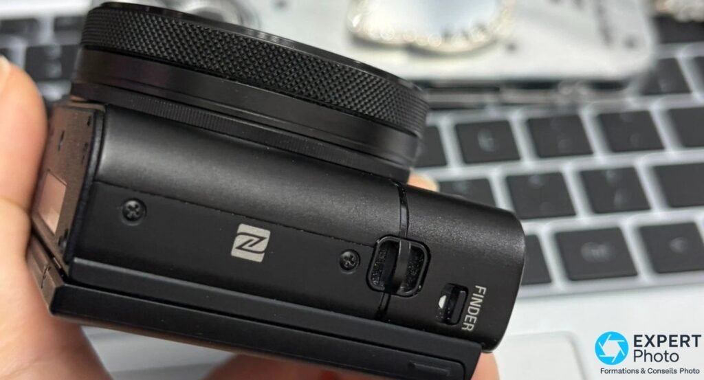 Profil gauche du Sony RX100 VA, logo NFC et marquage FINDER de la trappe du viseur escamotable, boîtier tenu en main