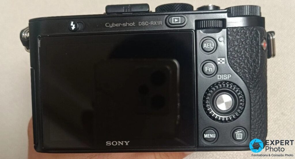 Sony RX1R de dos, écran LCD éteint : inscription « Cyber-shot DSC-RX1R », boutons AEL, Fn, DISP, MENU, molette de navigation