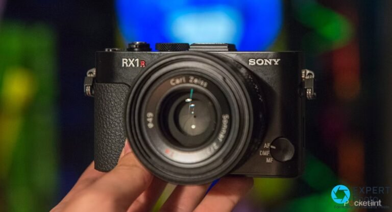 Sony RX1R vu de face en main : inscription RX1R en rouge, logo SONY, objectif Carl Zeiss, sélecteur AF/DMF/MF à droite