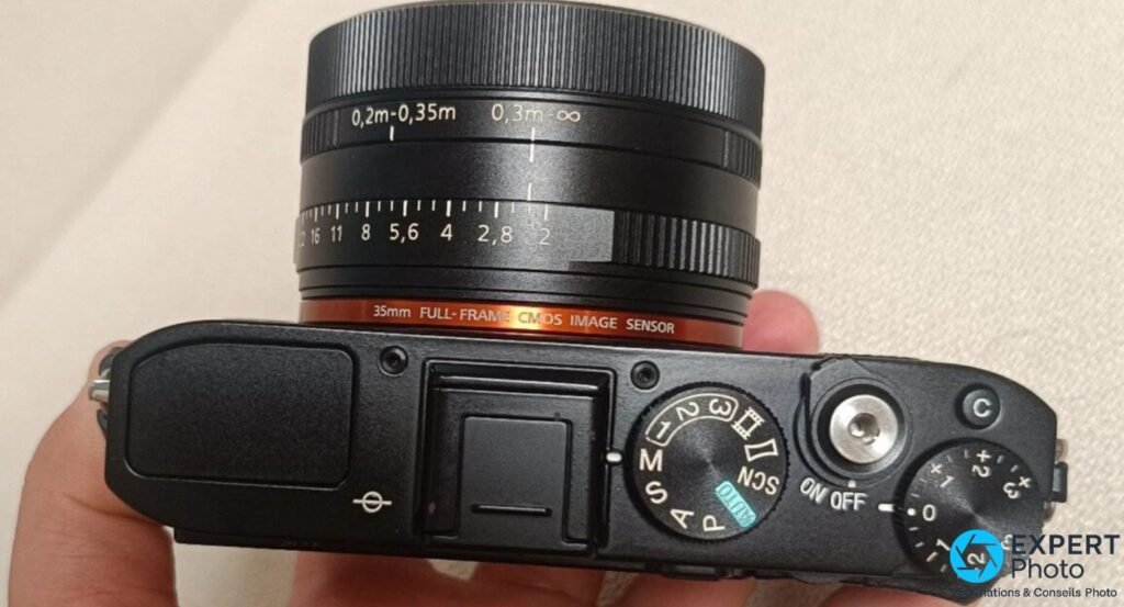 Sony RX1R vu de dessus, fond blanc : bague distance 0,2m–∞, bague diaphragme f/2 à f/16, molette modes M/S/A/P/SCN, ON OFF