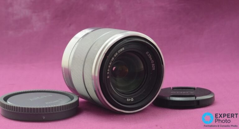 Sony E 18–55 mm OSS : un zoom de kit à garder ou à remplacer ? Sony E 18–55 mm OSS argenté couché en diagonale, face frontale visible, marquages E 3.5-5.6/18-55 OSS et Ø49 lisibles, caches avant et arrière noirs