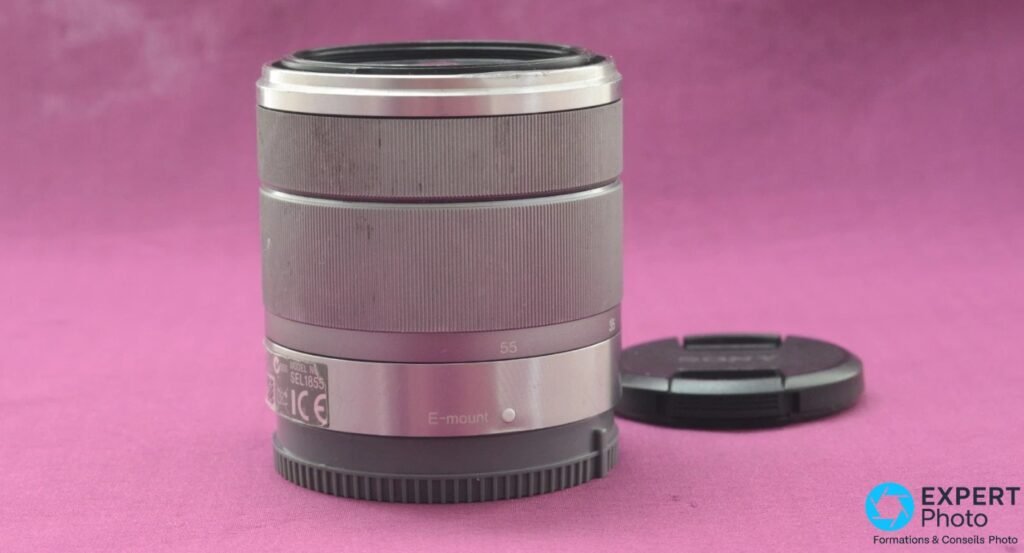 Flanc arrière du zoom Sony SEL1855, étiquette avec référence SEL1855 et inscription E-mount lisibles, cache avant noir posé à droite