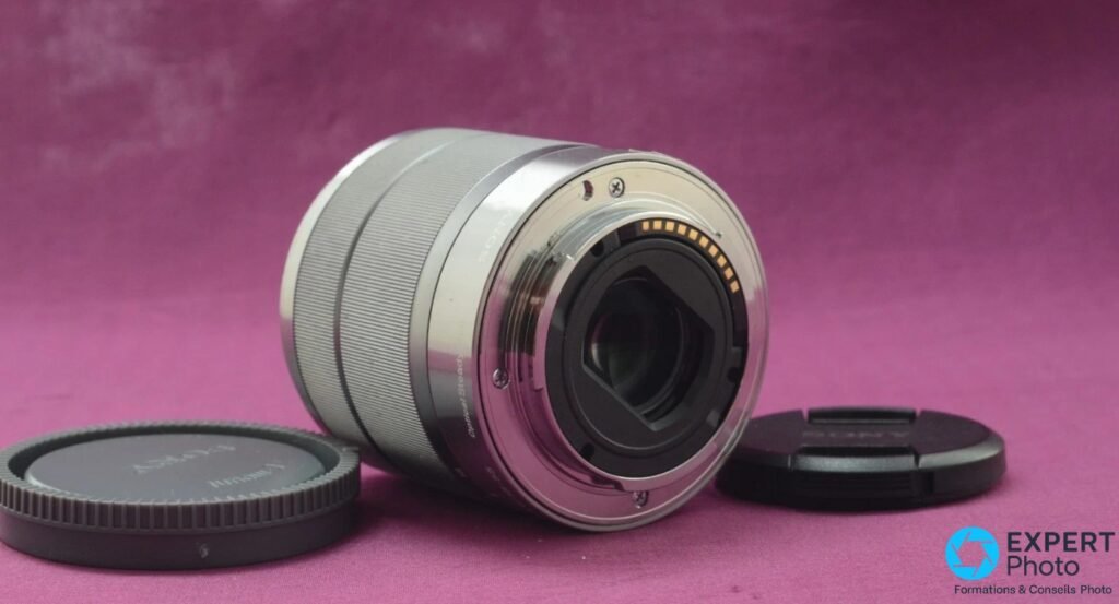 Monture arrière Sony E du zoom SEL1855, baïonnette argentée ouverte et contacts électriques dorés visibles, objectif couché en diagonale