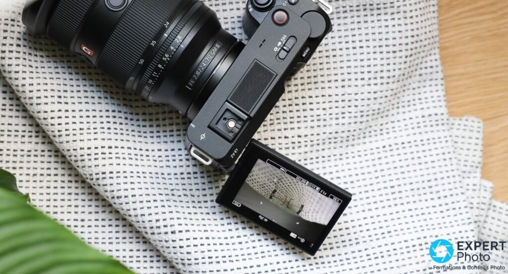 Sony ZV-E1 vu du dessus, écran déployé en position selfie montrant l'interface vidéo avec paramètres d'exposition, zoom FE 24-70 GM II monté