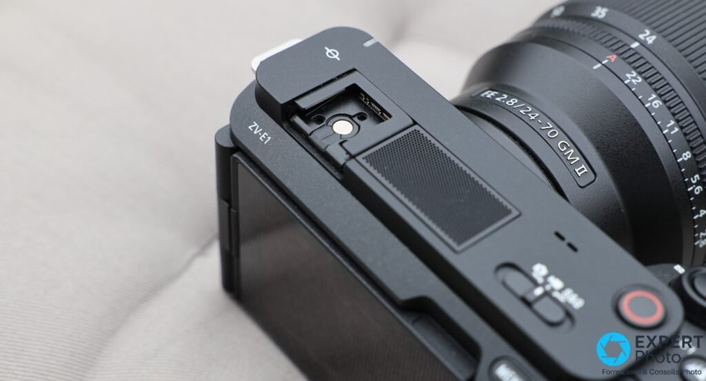 Sony ZV-E1 griffe multi-interface ouverte avec contacts dorés visibles, microphone intégré et objectif FE 2.8/24-70 GM II partiellement visible
