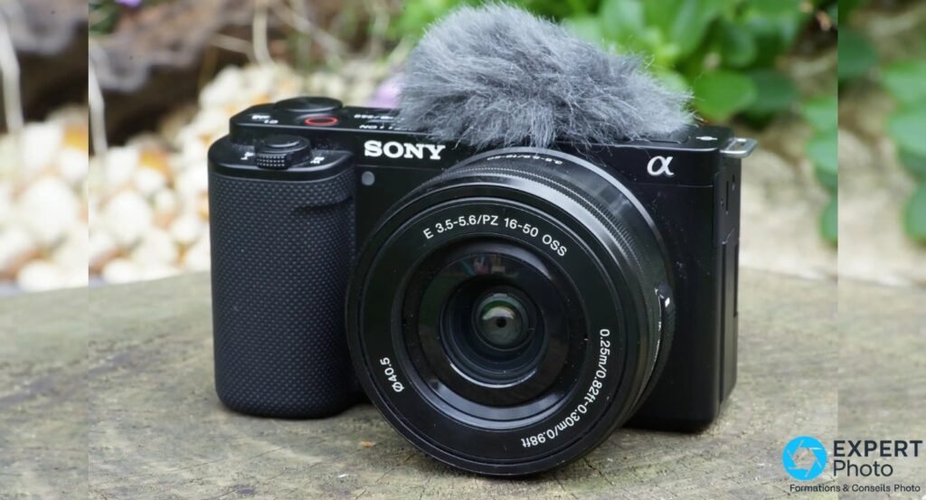 Sony ZV-E10 noir face avant, objectif E PZ 16-50 OSS, bonnette anti-vent grise sur micro intégré, posé sur pierre