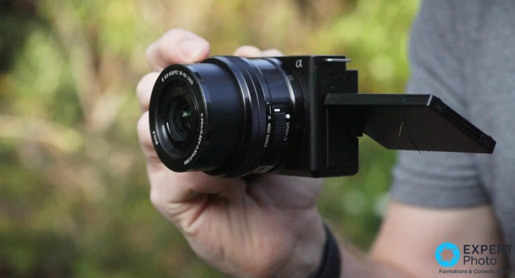 Main tenant le Sony ZV-E10 noir, objectif E PZ 16-50 OSS, écran orientable déployé en position vlog