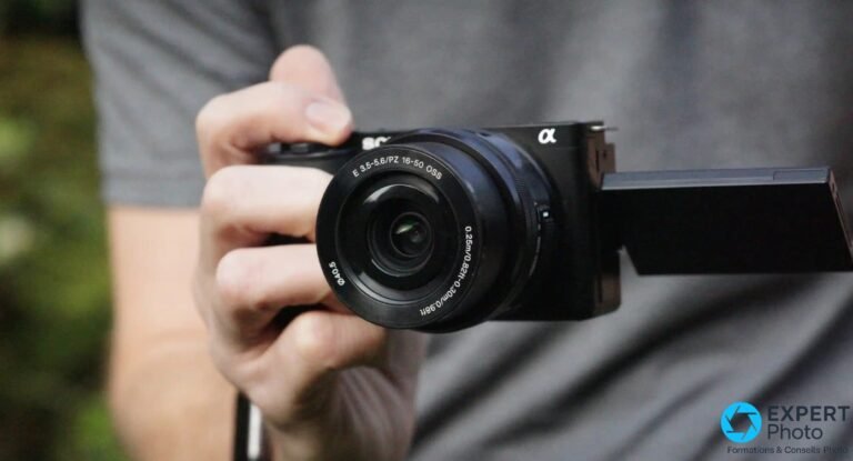 Main tenant le Sony ZV-E10 noir de face, objectif E PZ 16-50 OSS, écran orientable déployé en position selfie