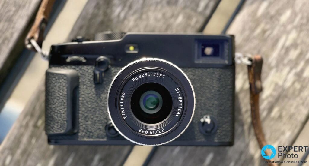 TTArtisan 23mm f/1.4 monté sur boîtier hybride compact noir posé sur bois, vue de face légèrement en plongée