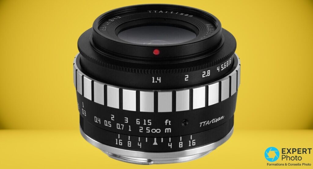 TTArtisan 23mm f/1.4 vue 3/4 avant sur fond jaune, graduations diaphragme 1.4 à 16 et distances lisibles 