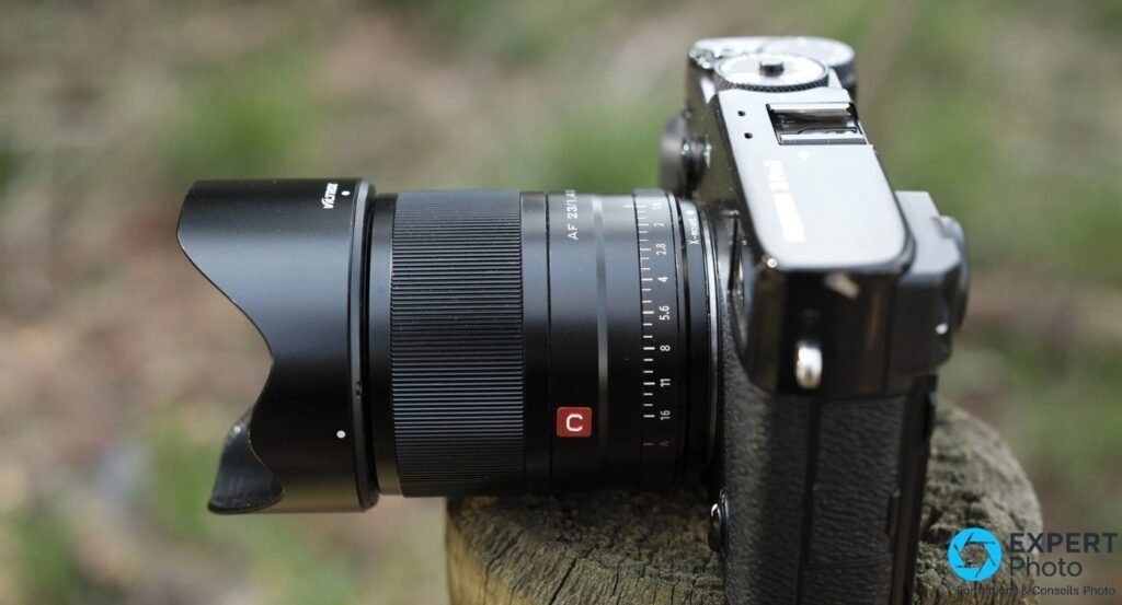 Viltrox AF 23mm f/1.4 XF avec pare-soleil tulipe, bague ouverture et pastille C visible, monté sur boîtier Fujifilm X, profil gauche
