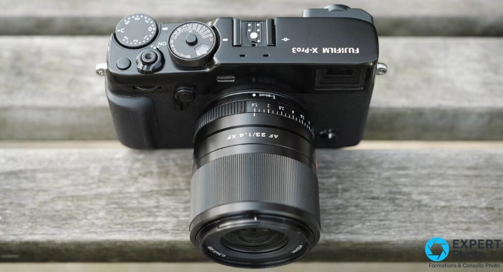 Viltrox AF 23mm f/1.4 XF sans pare-soleil, bague ouverture et molettes du Fujifilm X-Pro3 visibles, vue plongée sur lattes de bois