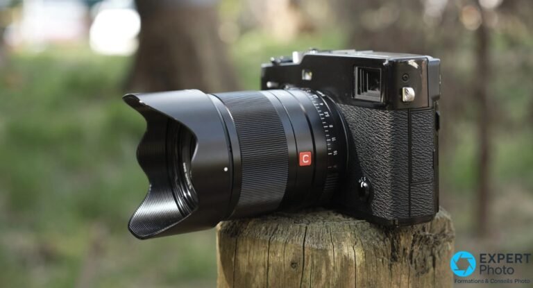 Avis Viltrox AF 23mm f/1.4 XF : ce que vaut ce 35mm lumineux sur Fujifilm X Viltrox AF 23mm f/1.4 XF avec pare-soleil tulipe, bague C visible, monté sur boîtier Fujifilm X noir, vue 3/4 avant sur souche