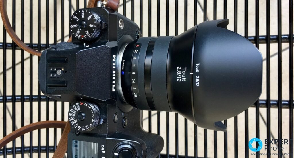 Zeiss Touit 2.8/12 sur Fujifilm avec bretelle cuir, vue dessus sur grille noire, bague Touit 2.8/12 lisible