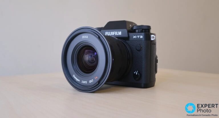 Test Zeiss Touit 12mm f/2.8 : pour les photographes APS-C engagés en focale fixe grand-angle Zeiss Touit 2.8/12 sur Fujifilm X-T3, vue 3/4 avant, lentille frontale Distagon T* visible, sans pare-soleil