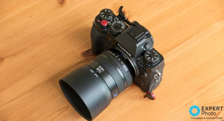 Zeiss Touit 32mm f/1.8 : rendu Zeiss sur APS-C, occasion et alternatives Fuji/Sony Zeiss Touit 32mm f/1.8 monté sur boîtier Fujifilm X-T1 noir, avec pare-soleil cylindrique, posé en diagonale sur bois